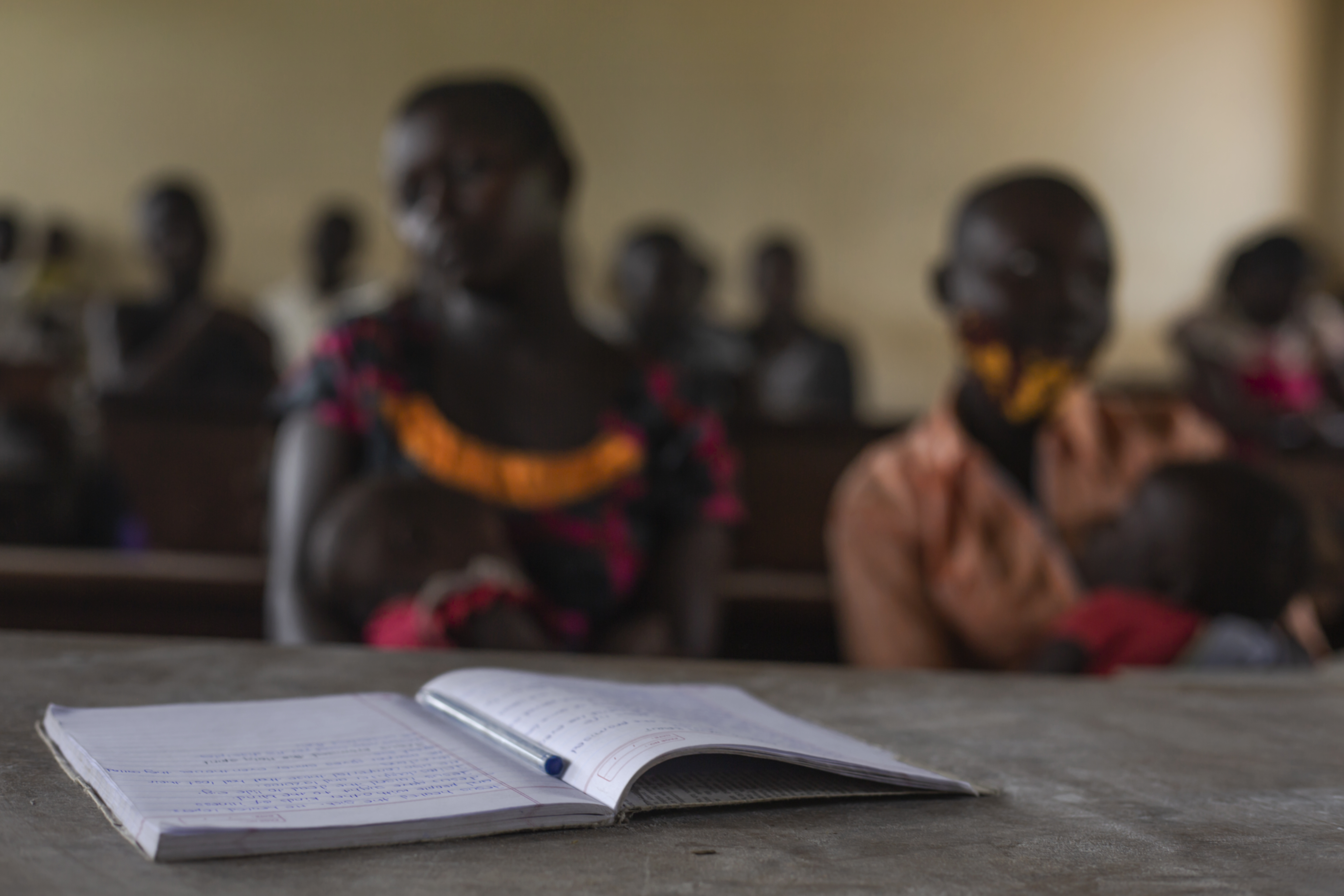 Pupils attend class at Ombaderuku Primary School, Ayivu Division, Arua District. In the background is a teenage mother attending the session with her child. The school, with a high number of teenage mothers, rising within the COVID19 lockdown has developed ways and strategies of encouraging the girls to continue with their studies.